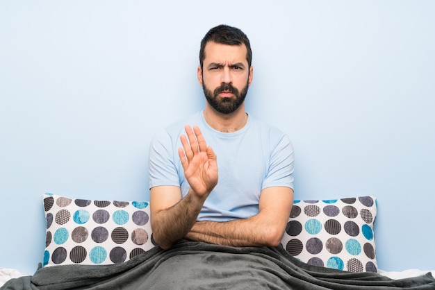 Hombre en la cama haciendo gesto de parada