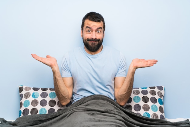 Hombre en la cama teniendo dudas al levantar las manos.