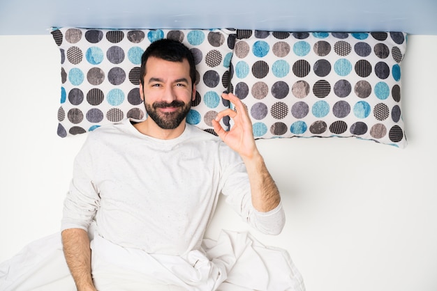 Hombre en la cama en la vista superior que muestra bien firmar con los dedos