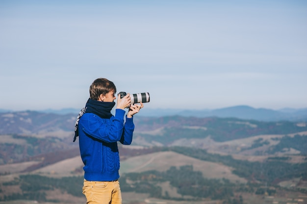 Hombre con una cámara en el borde de un acantilado con vistas a las montañas por debajo