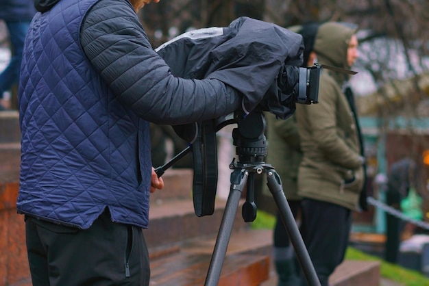 Hombre con una cámara de video impermeable cubierta filmando algo bajo la lluvia Cubierta negra Prensa exterior Pasión Protección Público Operador especial Producción Grabar Tv Video Tiempo húmedo