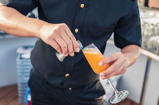 Hombre camarero mezclando cócteles con jugger vertiendo sobre copa de vino en el bar de la azotea
