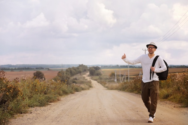 Un hombre camina por un camino rural. Autoestopista por todo el país. Un hombre detiene un automóvil que pasa por la carretera.