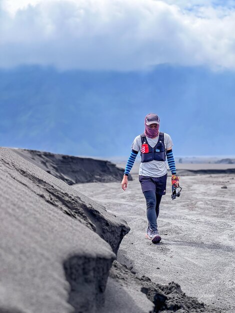 Foto un hombre camina por un camino de tierra con un cielo azul de fondo.