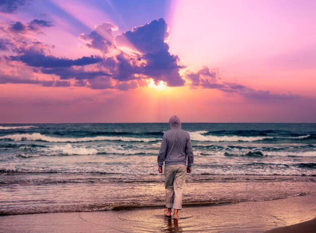 Un hombre camina descalzo por la playa y mira una puesta de sol mágica