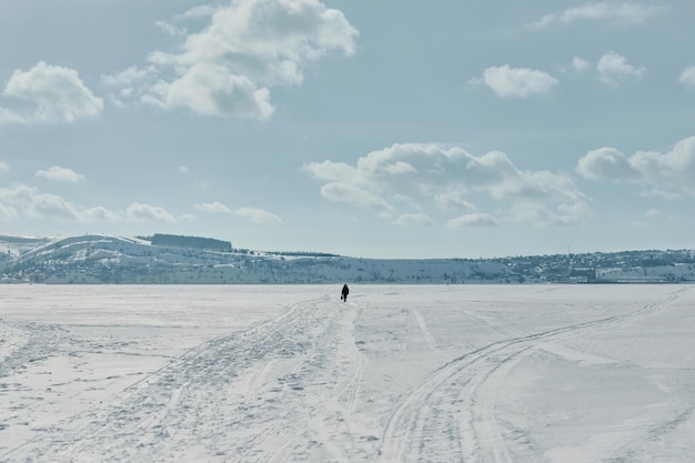 Un hombre camina a lo largo de un río congelado en invierno Paisaje invernal Mucha nieve Nieve y cielo