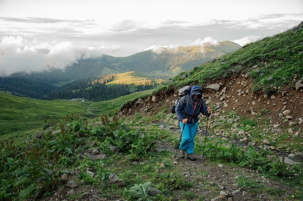 Hombre caminando por el camino de tierra con mochila de senderismo y palos en la colina