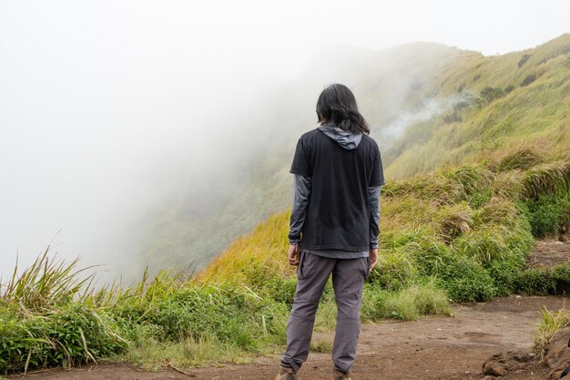 Hombre caminando a la cima de la montaña con la pista de Savana y vibraciones nubladas