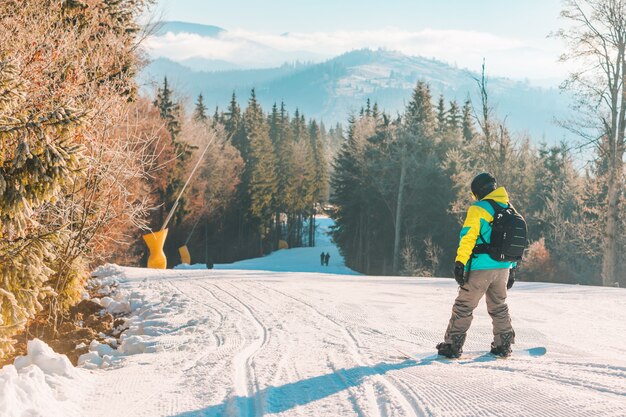 Hombre caminando por la colina con montañas de snowboard en el fondo