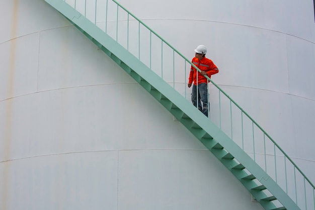 Hombre caminando por la escalera de inspección visual de aceite del tanque de almacenamiento