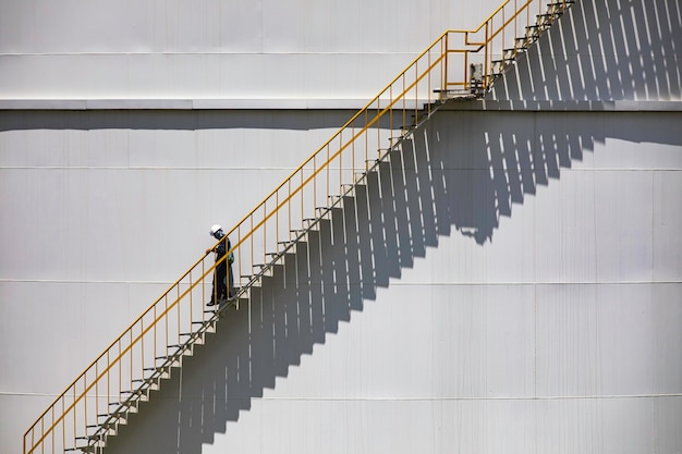 Un hombre caminando por las escaleras de aceite del tanque de almacenamiento de registros visuales de inspección de arriba en la placa lateral de la carcasa