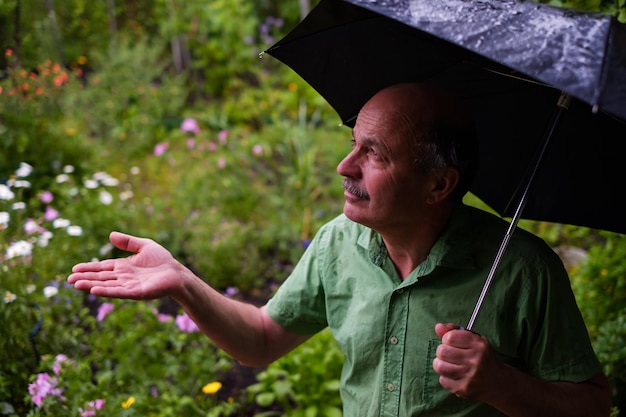 Hombre caminando en el jardín con sombrilla durante la lluvia