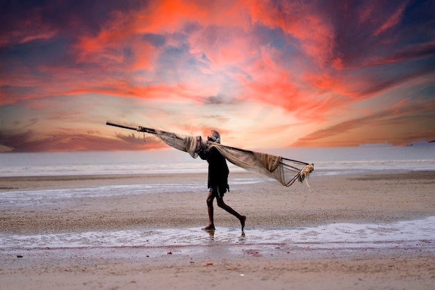 Un hombre caminando por la playa con un gran paño sobre la cabeza.