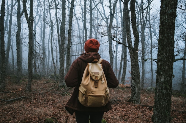 Hombre caminando por un sendero oscuro a través de un bosque tenebroso. Hipster con una mochila a la espalda se va de viaje