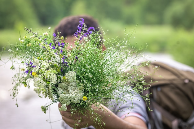 Un hombre en una caminata sostiene un ramo de flores silvestres sobre un fondo borroso.