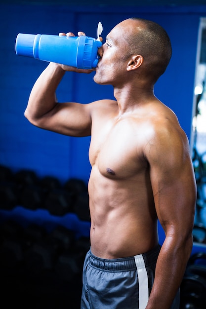 Hombre sin camisa, agua potable en el gimnasio