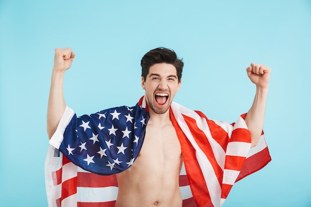 Hombre sin camisa alegre que se encuentra aislado, vistiendo la bandera americana, celebrando el éxito