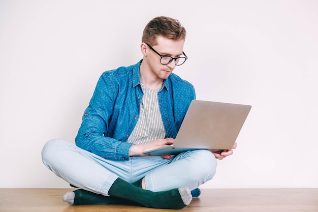 Hombre con camisa y anteojos trabajando en una computadora portátil sentado en la mesa sobre un fondo blanco