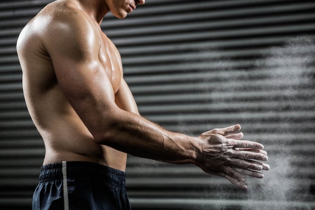 Hombre sin camisa aplaudiendo las manos con talco en el gimnasio de crossfit