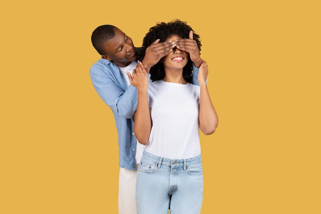 Hombre con una camisa azul cubriendo juguetón los ojos de una mujer sonriente para una sorpresa ambos en ropa casual