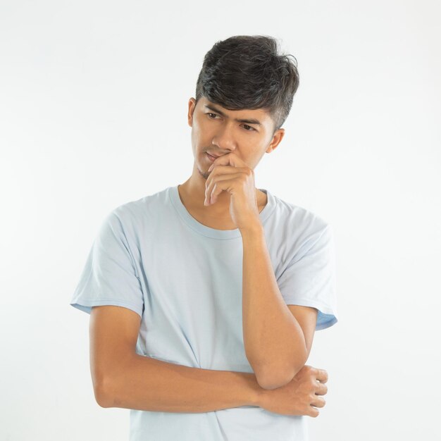 Un hombre con una camisa azul está de pie y tiene una mano en la barbilla.