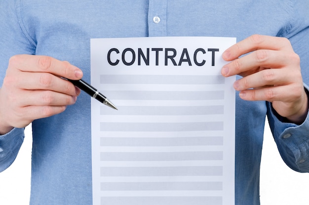 Un hombre con una camisa azul está sosteniendo una hoja con un contrato y una pluma sobre un fondo blanco.