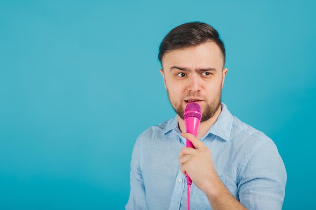 el hombre con camisa azul se para en el fondo azul y canta con un micrófono rosa