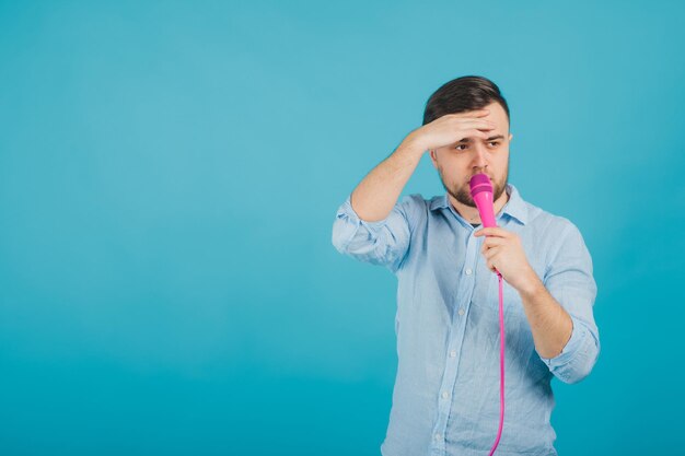 el hombre con camisa azul se para en el fondo azul y canta con un micrófono rosa