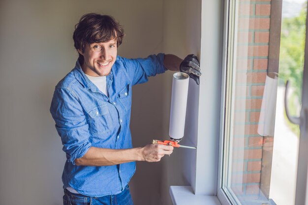 El hombre con una camisa azul hace la instalación de la ventana. Usando una espuma de montaje.