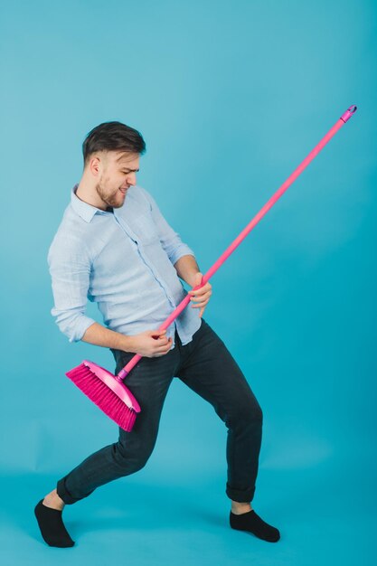 el hombre de camisa azul se para sobre fondo azul con escoba rosa