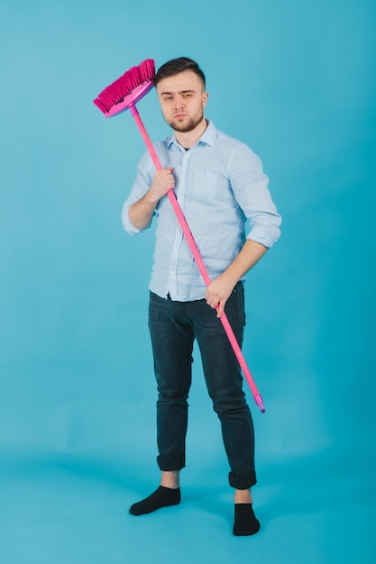 Foto el hombre de camisa azul se para sobre fondo azul con escoba rosa