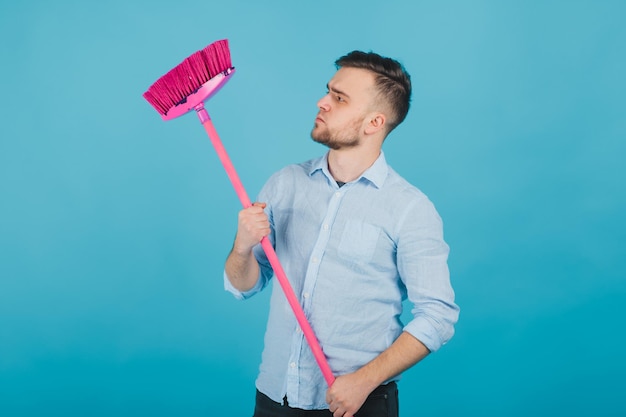 el hombre de camisa azul se para sobre fondo azul con escoba rosa