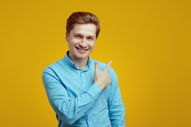 Hombre con camisa azul sonriendo y apuntando a la izquierda sobre la pared naranja