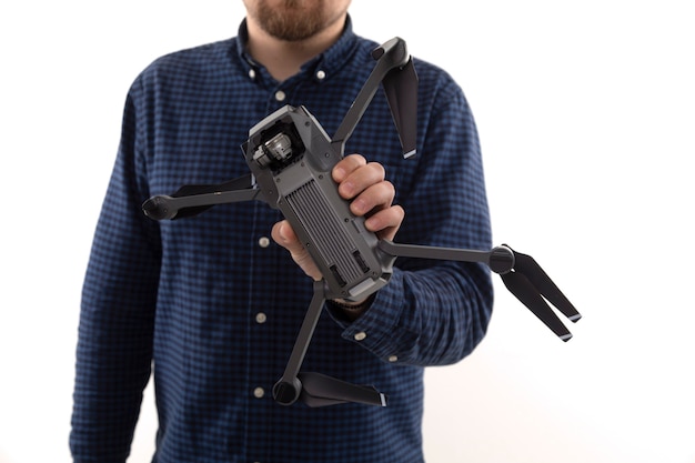 Un hombre con una camisa azul sosteniendo un quadcopter sobre un fondo blanco.