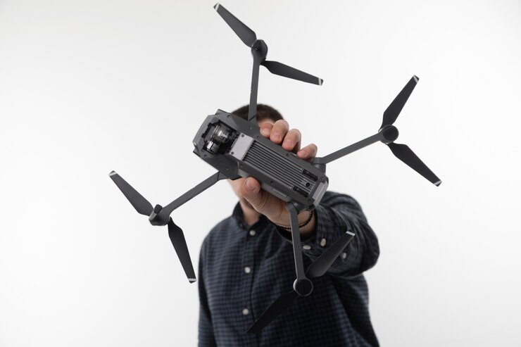 Foto un hombre con una camisa azul sosteniendo un quadcopter sobre un fondo blanco.
