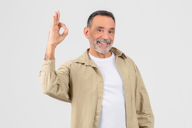 Hombre con camisa blanca y chaqueta bronceada haciendo una señal de "okay"