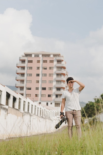 Un hombre con una camisa blanca y pantalones color canela se para frente a un edificio con un edificio al fondo.