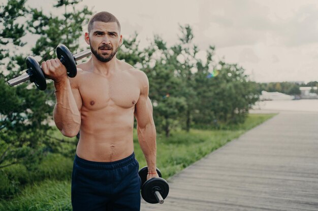 Foto hombre sin camisa confiado levantando pesas en el parque