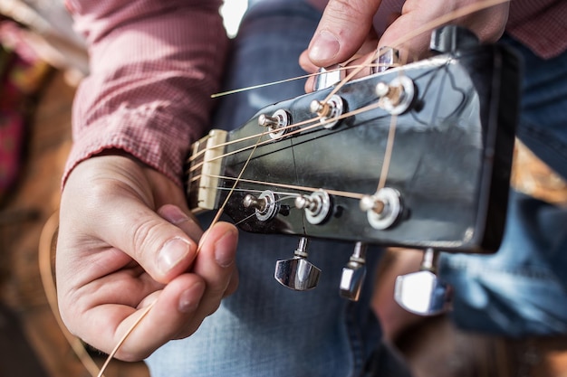 Un hombre con una camisa a cuadros tira de nuevas cuerdas de guitarra cerca de la guitarra acústica