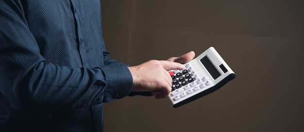 Un hombre con una camisa cuenta con una calculadora sobre una superficie marrón