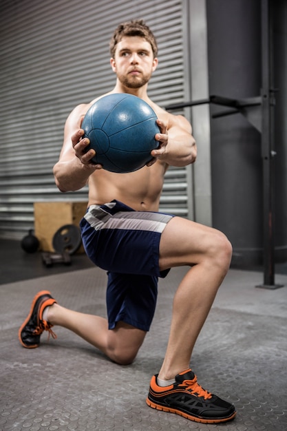 Hombre sin camisa entrenando con balón medicinal en el gimnasio