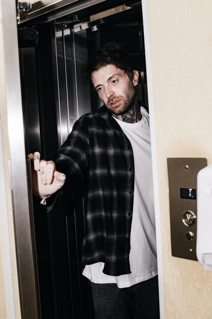 Foto un hombre con una camisa de franela está parado en una puerta con una mano apuntando a la puerta.