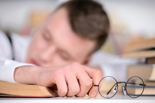 Hombre en camisa y gafas para dormir en la biblioteca.