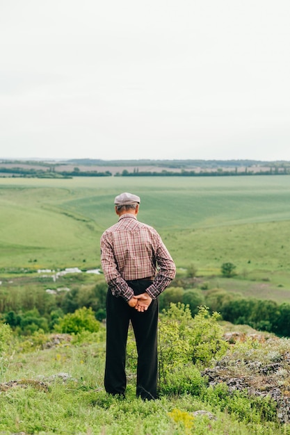 hombre con camisa y gorra camina por la montaña parado en una colina mirando el hermoso paisaje