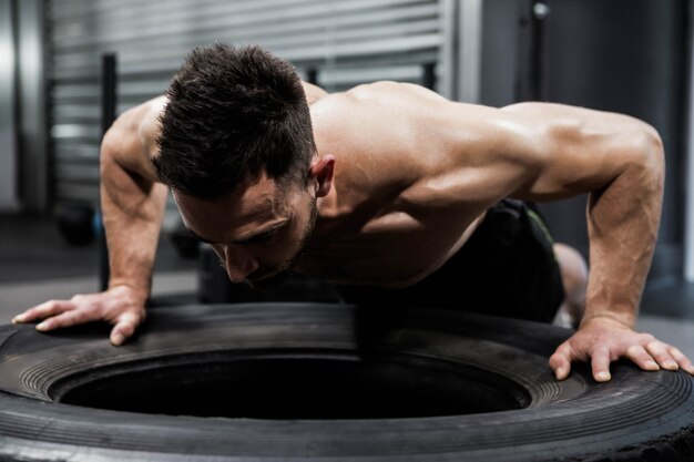 Hombre sin camisa haciendo flexiones en un neumático pesado en el gimnasio de crossfit