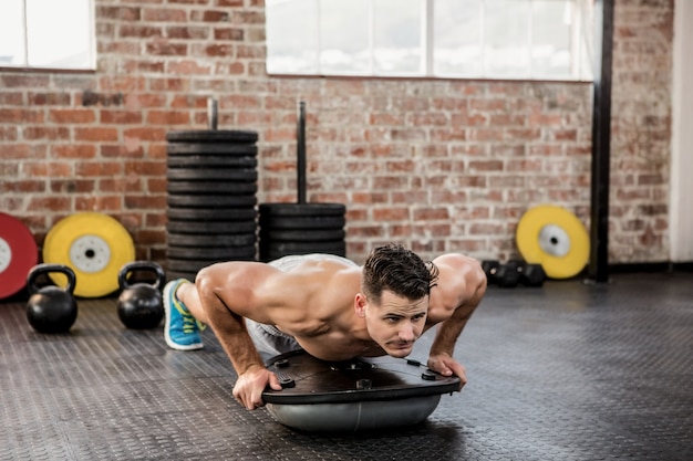 Hombre sin camisa haciendo push ups bosu