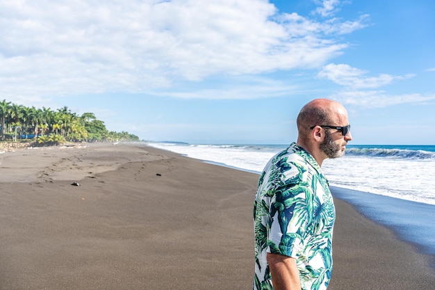 Hombre con una camisa hawaiana caminando por una playa tropical