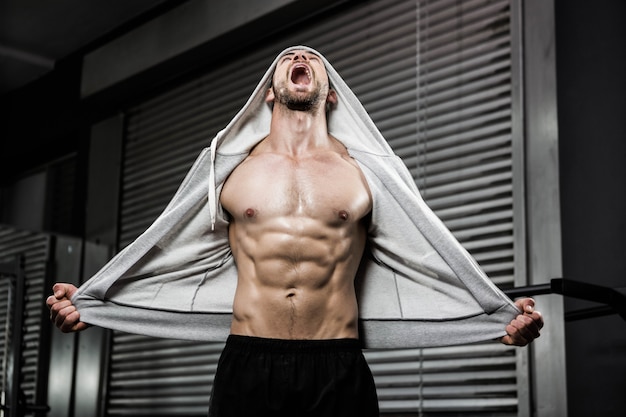 Hombre sin camisa con jersey gris gritando en el gimnasio de crossfit