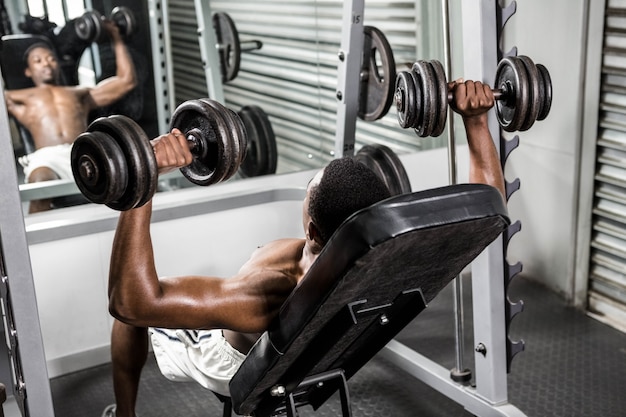 Hombre sin camisa levantando pesas en el banco en el gimnasio de crossfit