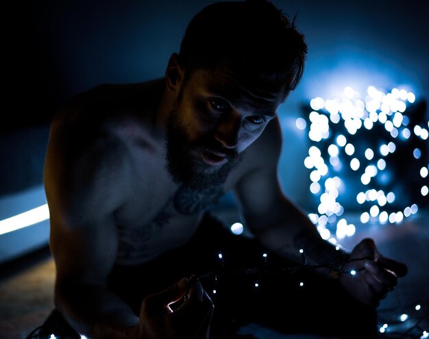 Foto hombre sin camisa con luces de cuerda iluminadas en la oscuridad